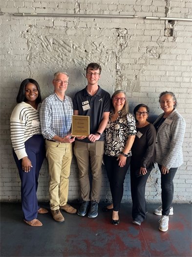Photo of the BioReady team standing in front of a rustic brick wall. The two in the middle are holding the BioGeorgia BioReady plaque.