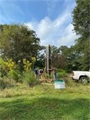 Three men installing a approximately 15 ft wooden Chimney Swift tower on a sunny day in a wildflower field at Dudley Park