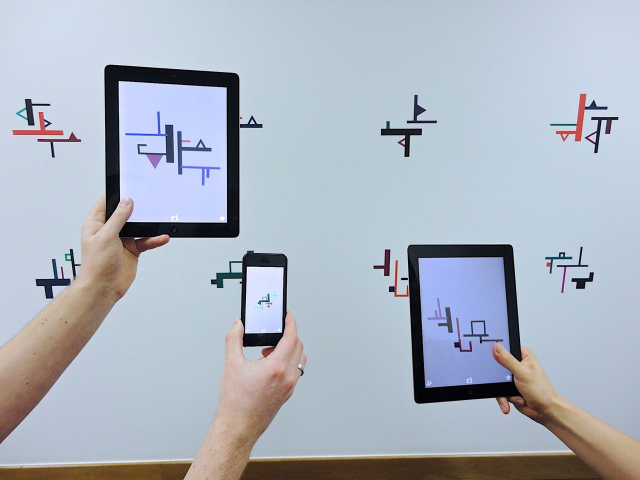 Arms holding tablets taking photos of art on wall.