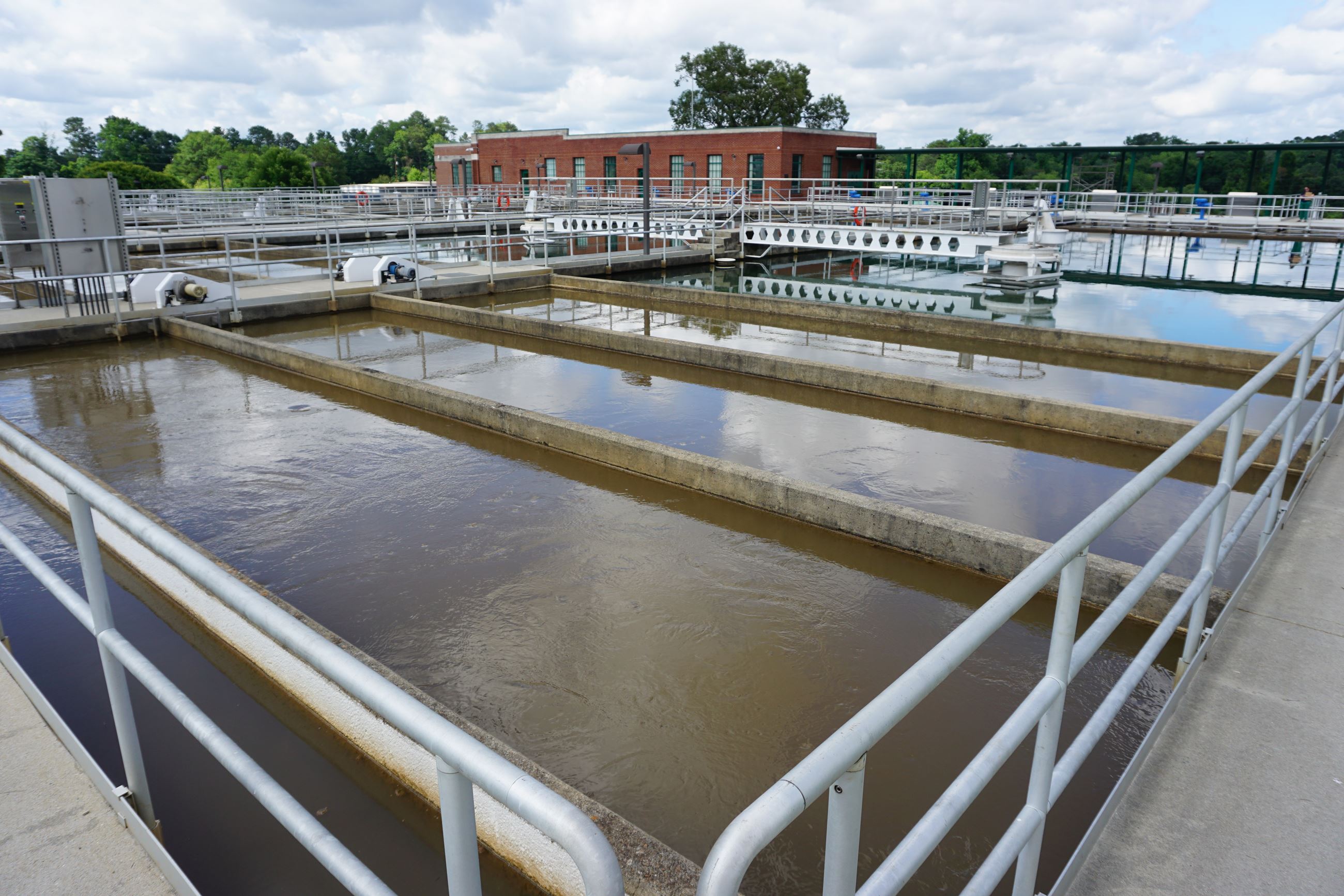 Safety Bars in front of several pools of water, seperated by concrete walls. Brick Building in back.